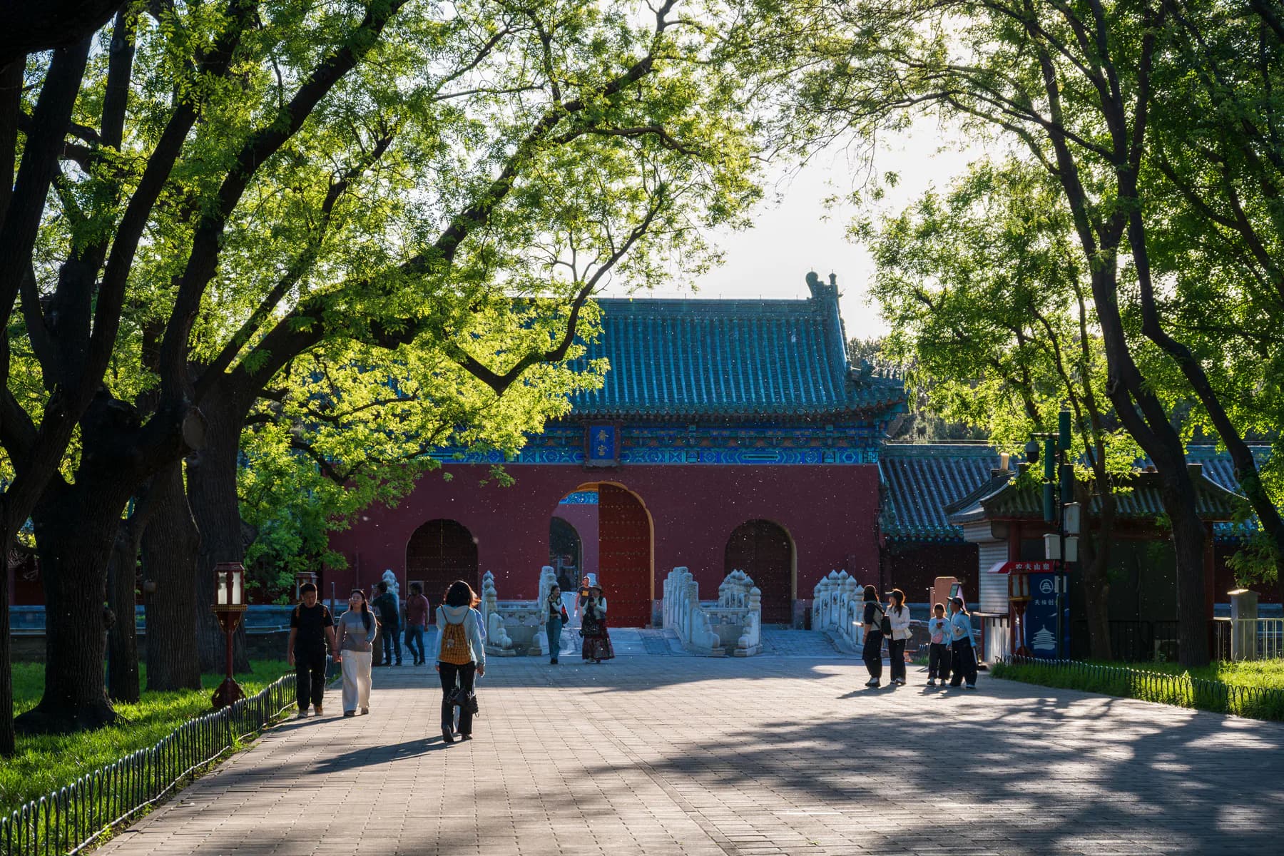 Visitors walking through a shaded historic Beijing temple courtyard