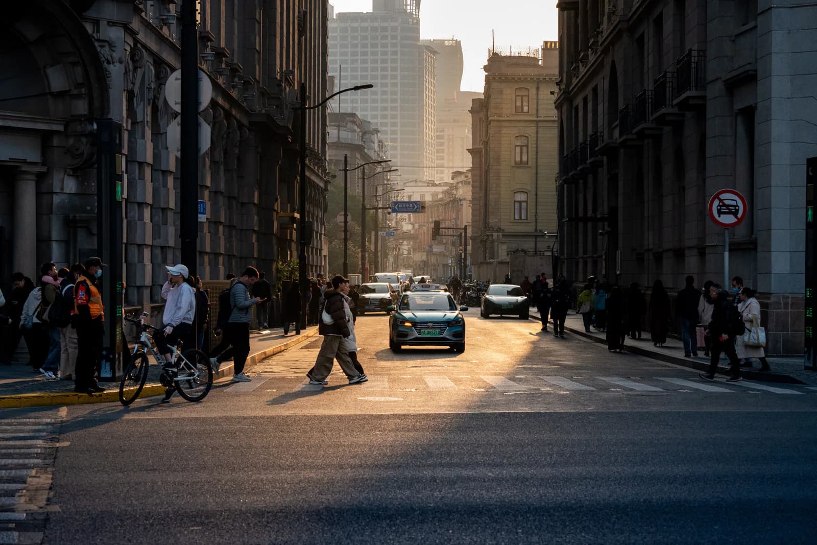 Pedestrians, cyclists and taxis crossing a sunlit historic Shanghai street