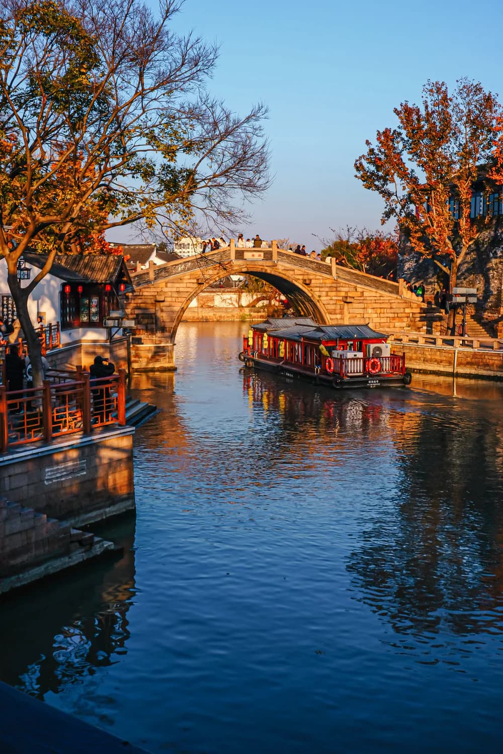 A canal boat approaching a stone arch bridge in autumnal Suzhou
