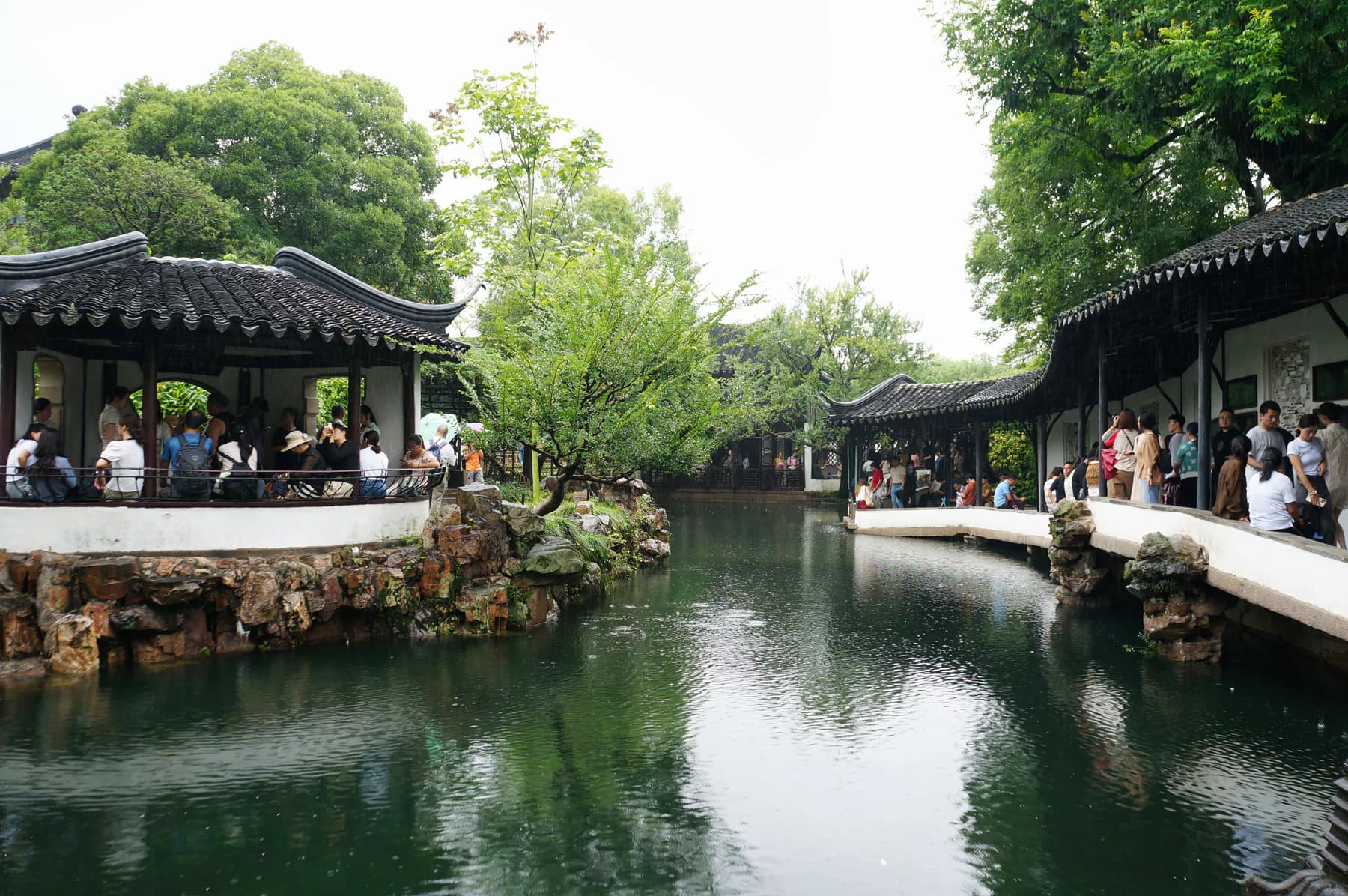 Visitors moving through layered corridors around a classical Suzhou garden pool